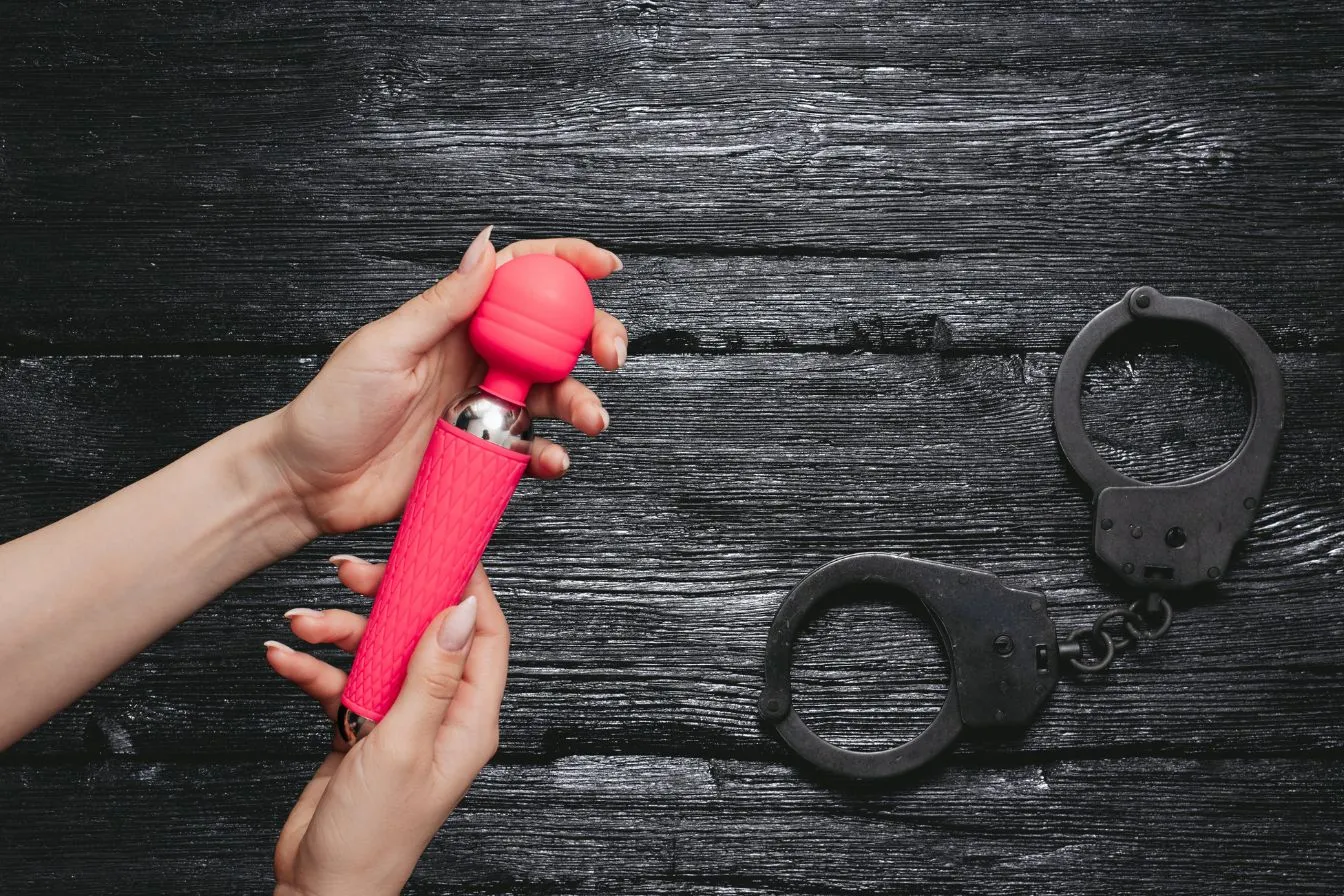 une femme tient un sextoy vers des menottes