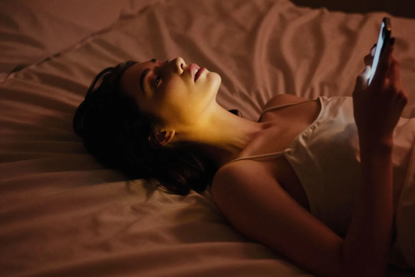 Femme dans une ambiance intime le soir, smartphone à la main, illustrant les échanges érotiques en ligne entre adultes