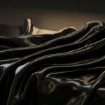 Gros plan sur un tissu noir brillant effet wetlook drapé avec des reflets lumineux.