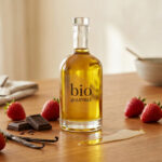 Une bouteille d'huile bio gourmet entourée de fraises, de carrés de chocolat, de gousses de vanille et de menthe fraîche.