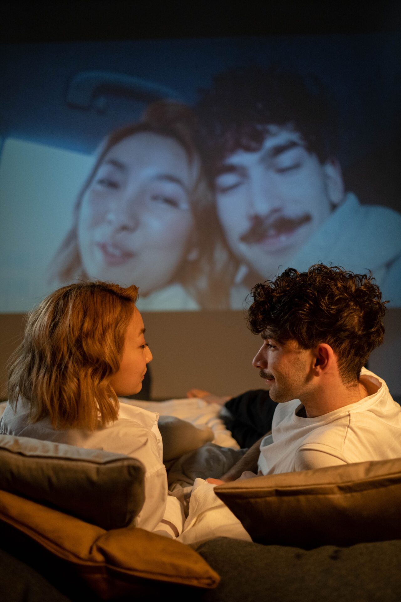 Un couple allongé se regarde et se parle, une projection lumineuse derrière eux